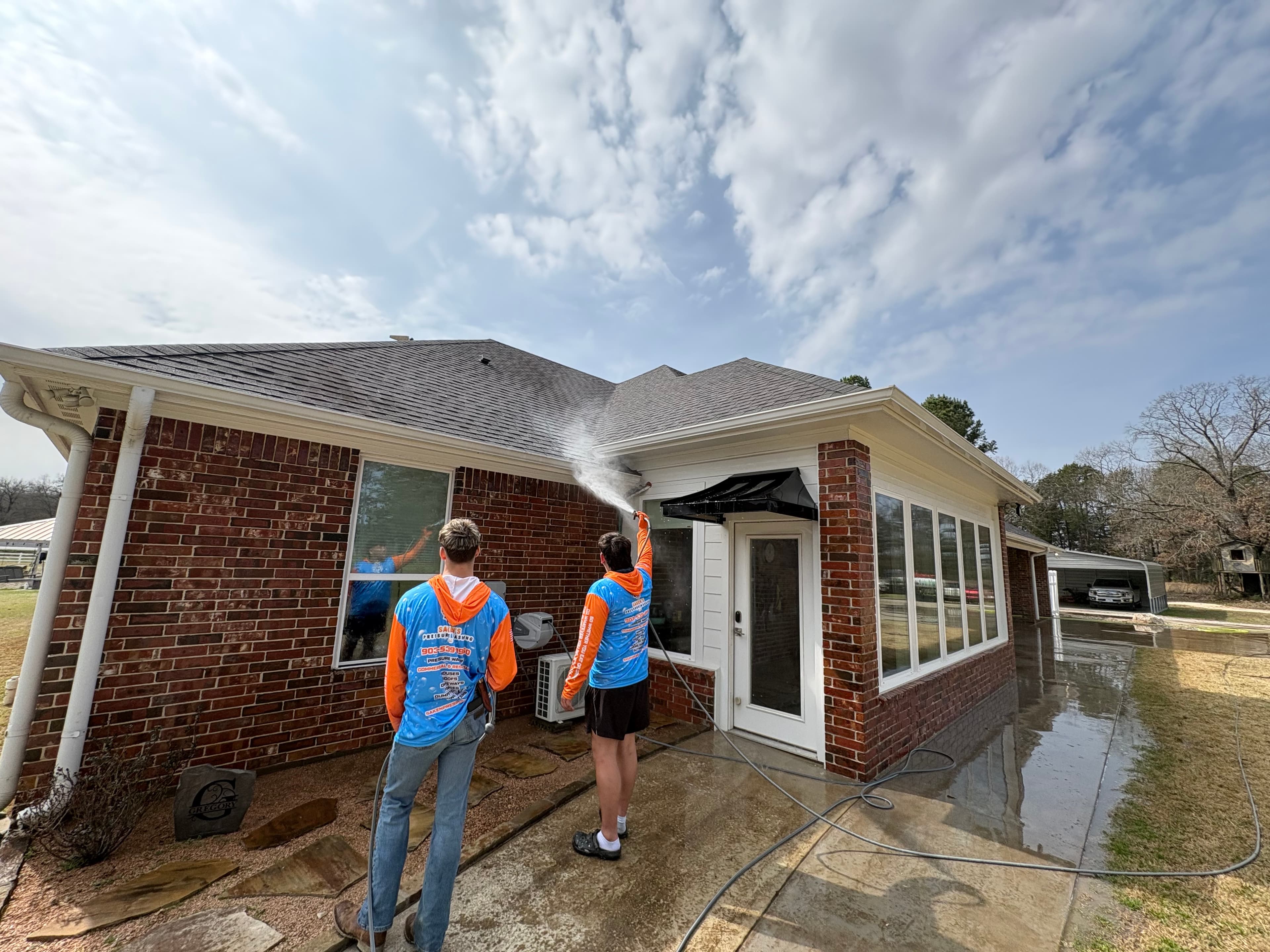 Two crew members washing the brick exterior and windows of a house